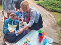 Uczeń siedzi na wózku i wkłada niebieski przedmiot do niebieskiego kubka który trzyma nauczyciel 
