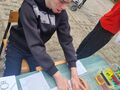 Uczeń siedzi przy stole i z pomocą nauczyciela odpina ramkę z rzepami 