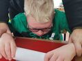 3. Chłopiec z pomocą opiekuna wałkuje glinę 