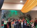 Grupa dzieci z nauczycielami śpiewają na scenie piosenkę