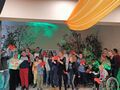uczniowie i nauczyciele stoją na scenie i trzymają w rękach czerwone serca z papieru