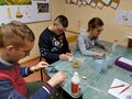dzieci siedzą w ławkach i przygotowują małe ekochoinki z tektury i koronki