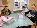 uczniowie siedzą w klasie przy stole i wykonują eksperyment z krystalizacją solimieszją w słoiku wode z sola