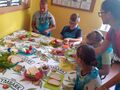 Zdjęcie 5 klasa przygotowuje kanapki siedząc przy stole obok pomaga nauczycielka