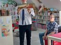 Zdjęcie przedstawia chłopców którzy są w bibliotece. Jeden z uczniów trzyma w rękach książkę 