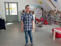 Zdjęcie przedstawia stojącego chłopca który recytuje wiersz. Uczeń jest w bibliotece 
