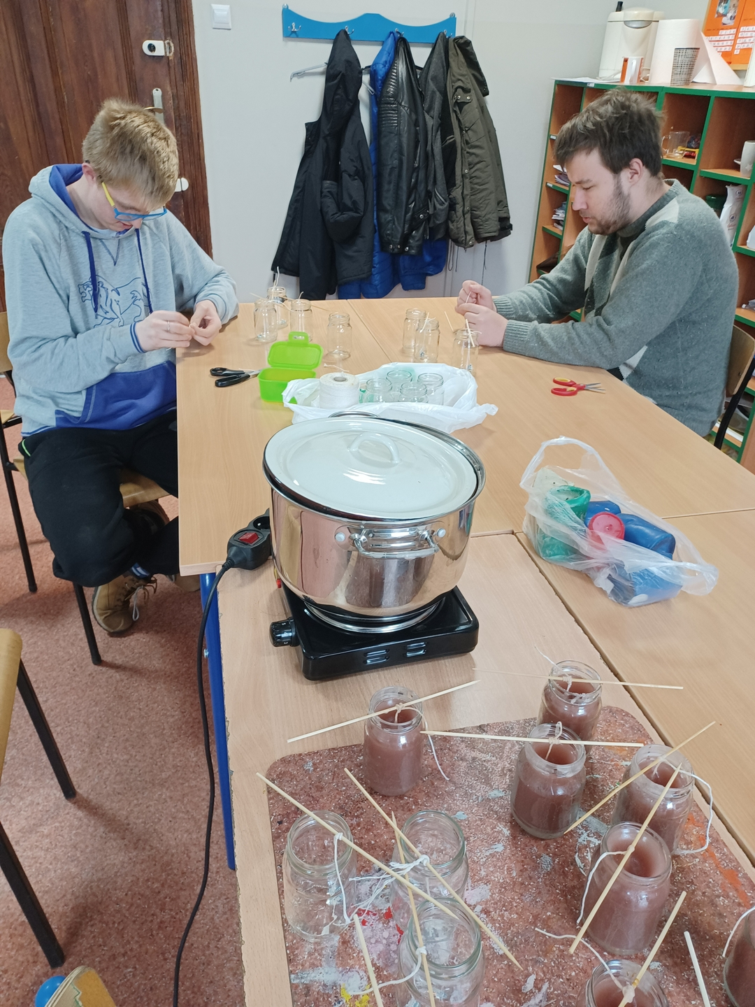 17. Na pierwszym planie widać słoiczki z woskiem oraz przenośną kuchenkę elektryczną na której w garnku podgrzewany jest wosk. W tle widać uczn