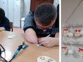 13. Dwóch uczniow siedzi przy szkolnych ławkach posługują się wypalarkami do drewnawypalają wzory w drewnanych sklejkach w kształcie bombek. O
