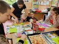 2. Nauczycielka pomaga uczniowi kroić paprykę obok siedzą inne dzieci 