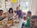 Uczniowie siedzą przy stole urodzinowym mama ucznia kroji tort
