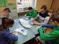 uczniowie siedzą w klasie w ławce i kazdy do swojego pojemnika wkada watę