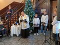 1.wizyta duszpasterska w holu ośrodka ksiądz czyta Pismo Święteuczniowie i ministranci stoją w tle stół nakryty białym obrusem krzyż i świec