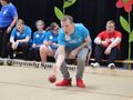 chłopiec toczy kulę do bocce z tyłu siedzą zawodnicy na ławce