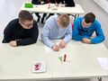 2. Uczniowie siedzą przy stoliku rozwiąują zadania na kartce w tle jury 