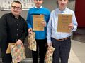 4. Trzej chłopcy stoją uśmiechnięci trzymają w rękach dyplomy i nagrody 