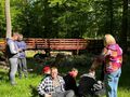 uczniowie siedzą na trawie w lesie obok stoi nauczycielka