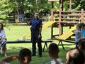 uczniowie siedzą na ławkach w parku i słuchają pani policjantki która stoi i mówi w tle zjeżdżalnie
