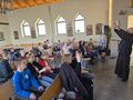 uczniowie na rekolekcjach w kościele siedzą i wykonują gesty do piosenki