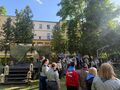zaproszeni goście i harcerze wspólnie śpiewają i wykonują pląsy stoją w kole wokół ogniska w parku w tle budynek szkoły obok scena