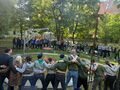 zaproszeni goście i harcerze wspólnie śpiewają i wykonują pląsy stoją w kole wokół ogniska w parku z tyłu w oddali widać stajnię