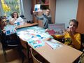 Uczniowie siedzą w ławkach pokazują zdjecia 0