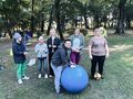 Chłopiec ćwiczy na piłce a reszta osób zanim go dopinguje. 