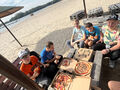 Uczniowie jedzą pizzę pod parasolami na plaży