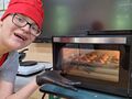 uczeń usmiecha sie przed piekarnikiem w którym znajdyją sie zrobione przez uczestników mufinki