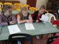 Uczennice siedzą przy ławkach w klasie i wypełniają karty pracy