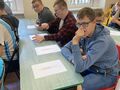 Uczniowie siedzą przy ławkach w klasie i wypełniają karty pracy