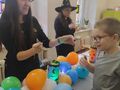 3 nauczycielki w kapeluszach stoją przy stole obok uczeń na stole balony