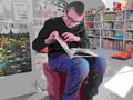 uczeń siedzi na pufie w bibliotece i czyta książkę