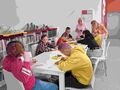 uczniowie siędzą przy stole w bibliotece i kolorują obrazki