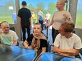 Trzech chłopców spędza czas przy stole a za nimi stoi opiekunka a obok niej chłopiec. Za namiotem trwają zaś rozmowy opiekunki z podopiecznymi