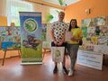 laureat konkursu pozuje do zdjęcia z opiekunem na tle prac konkursowych w holu ośrodka