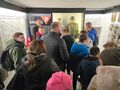 uczniowie i nauczyciele stoją i oglądają wystawę poświęconą kapłanom którzy zginęli w obozie koncentracyjnym w Dachau