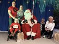 1 Rodzice z chłopcem obok świętego mikołaja z prawej strony nauczycielki wszyscy na scenie w tle niebieska płachta z gwiazdkami