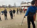 Nauczyciel pokazuje ćwiczenia z części kształtującej z wykorzystaniem kijków do nordic walking. 