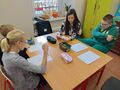 uczniowie siedzą przy ławce w klasie i słuchają czytanej bajki