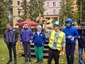 7. Uśmiechnięci uczniowie stoją pod sceną obok nich nauczyciel w okularach przeciwsłonecznych i niebieskim kapeluszu w tle scena 