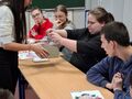 uczniowie siedzą przy ławkach w klasie i losują kartki
