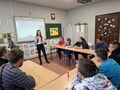 uczniowie siedzą przy ławkach w klasie i oglądają obrazek przedstawiony przez nauczyciela
