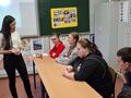 uczniowie siedzą przy ławkach w klasie i rozmawiają z nauczycielem