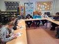 uczniowie siedzą przy ławkach w klasie i wykonują pracę grupową
