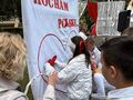 Dziewczynka z pomocą nauczyciela przyczepia czerwone serce wdzięczności na białym tle