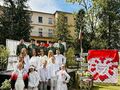 Grupa uczniów i nauczycieli z harcerzami występującymi na akademii stoją przed sceną na tle patriotycznej dekoracji