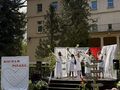 Uczniowie i nauczyciele ubrani na biało tańczą na scenie z gałązkami bzu