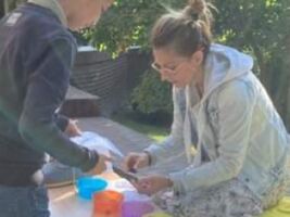Pani Anna Waśkowiak segreguje razem z uczniem obrazki, do kolorowych miseczek. Praca odbywa się przy stole w plenerze. U góry zdjęcia napis: Anna Waśkowiak