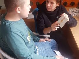 Pani Magdalena Faustyniak pokazuje obrazek z żyrafą, a uczeń nazywa co widzi. Siedzą przy stole. U góry zdjęcia napis: mgr Magdalena Faustyniak