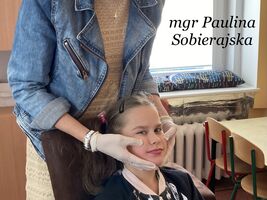 Uczennica siedzi na krześle, pani Paulina Sobierajska wykonuje masaż logopedyczny. U góry zdjęcia napis: mgr Paulina Sobierajska
